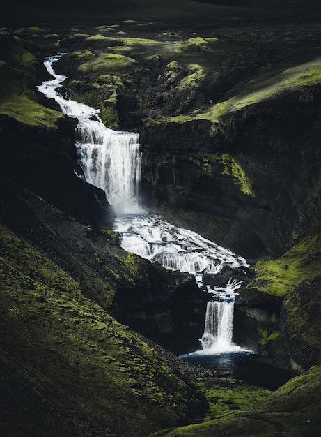 Fascinante toma vertical de un río con cascadas que fluyen sobre las montañas verdes