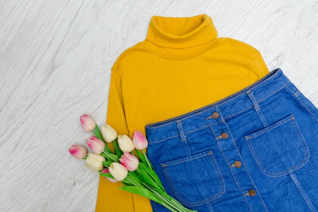 Fashion-Konzept. Gelber Rollkragenpullover, blauer Rock und rosa Tulpen. Holz Hintergrund