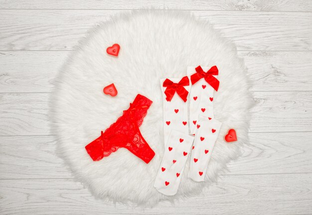Fashion-Konzept. Roter Tangahöschen und weiße Strümpfe mit Schleifen, Kerzen in Form eines Herzens auf einem weißen Pelz