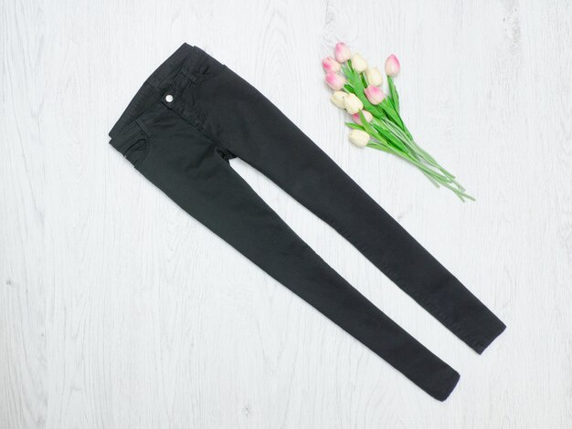 Fashion-Konzept. Schwarze Jeans und rosa Tulpen. Holz Hintergrund