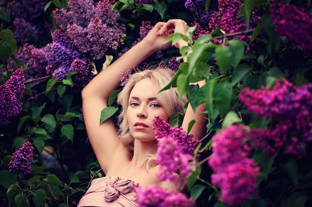 Fashion Spring Model Girl mit blonder Frisur. Sommer-schöne Frau mit dem gesunden und Schönheits-Haar, das Spaß auf Blumen-Hintergrund hat.