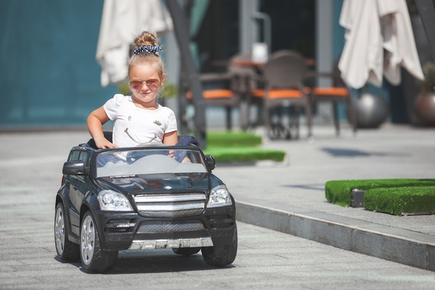 Fashionista de menina bonita fazendo compras com sacolas de compras. filho bonito ao ar livre no carro de brinquedo