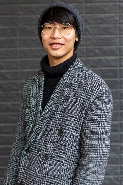 Foto fasionable atractivo hombre asiático vistiendo abrigo, sombrero, gafas sonriendo. ciudad urbana