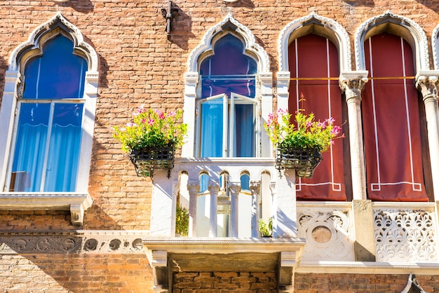 Fassade des alten Gebäudes mit typisch venezianischen Fenstern und weißem Balkon mit Blumentöpfen. Venedig, Italien