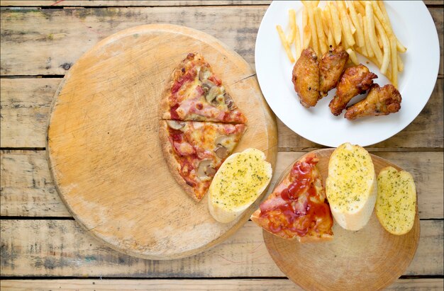 Fast food, asas de frango crocante, pão, batata frita e pizza em fundo de madeira