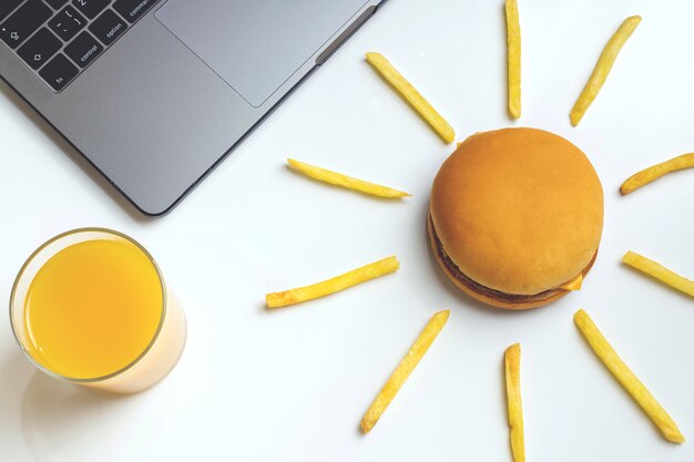 Fast Food bei der Arbeit Snacks. Laptop, Hamburger und Pommes Frites am Arbeitsplatz.