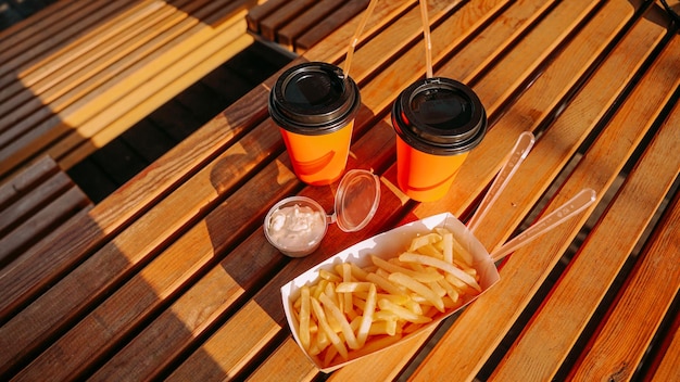 Fast food dois copos de papel laranja e batatas fritas com molho na mesa de madeira