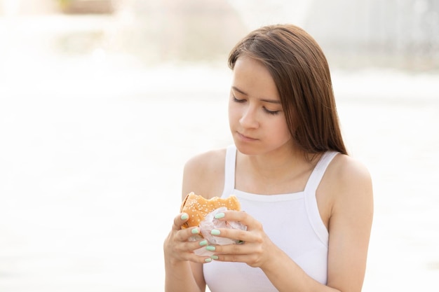 Fast Food ein Teenager-Mädchen im Park hat einen Burger