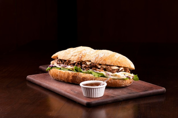 Fast-Food-Rinderbrustsandwich mit Rucola und Krautsalat auf Baguettebrot auf Holzbrett mit dunklem Hintergrund der Barbecue-Sauce