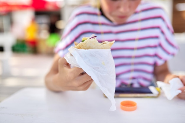 Fast-Food-Sommer-Lifestyle-Teenager Teenager-Mädchen, das einen Sandwich-Burger isst und auf den Smartphone-Bildschirm in Kopfhörern schaut