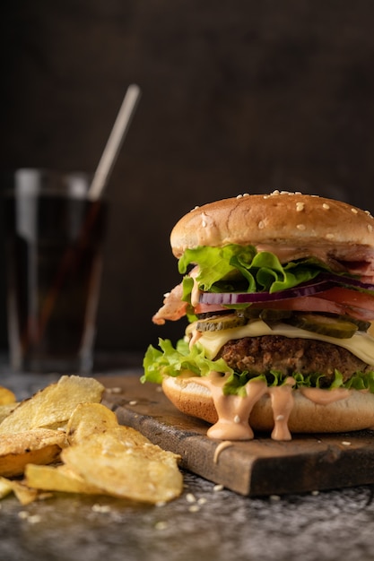 Fastfood. ein großer saftiger Burger mit Rinderpatty, Eisbergsalat, Tomaten, Gurken, Zwiebeln und Sauce und Speckscheiben. Zurückhaltend, dunkle Stimmung