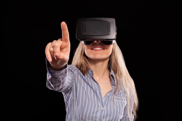 Faszinierte Frau, die ein Virtual-Reality-3D-Headset trägt und das Spiel auf schwarzem Hintergrund erkundet