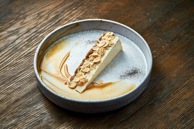 Fatia clássica de cheesecake com molho de amêndoas e caramelo, servida em prato branco sobre mesa de madeira. Comida do restaurante. Sobremesa apetitosa