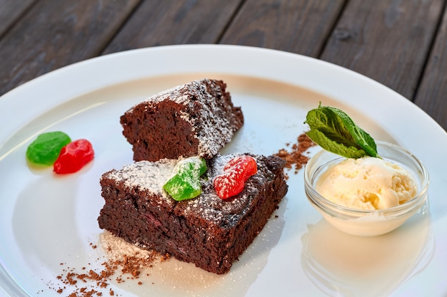 Fatia de bolo de chocolate com frutas cristalizadas, hortelã e sorvete em um prato