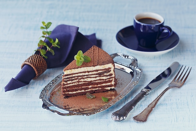 Fatia de bolo de chocolate delicioso em uma placa de prata com hortelã fresca no fundo da mesa de madeira azul claro.