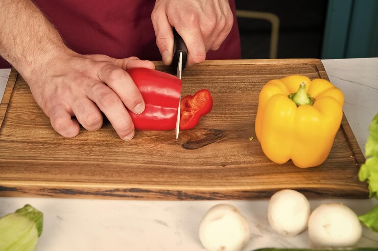 Foto fatia de pimenta de mão com faca de cerâmica legumes sendo cortados na tábua de madeira preparação de alimentos e receitas culinárias menu vegetariano e dieta saudável conceito de produtos orgânicos