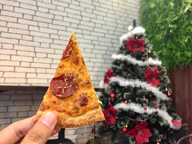 Fatia de pizza à mão com fundo de decoração de árvore de Natal