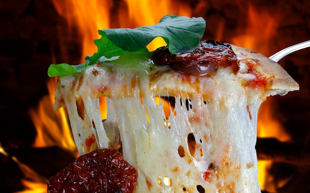 Fatia de pizza quente com derretimento de queijo com forno a lenha no fundo.