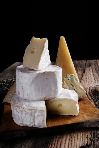 Foto fatia de queijo de camembert de cabra e brie na mesa de madeira escura