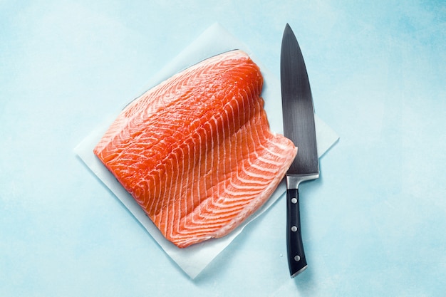 Fatia de salmão fresca em uma tábua de madeira com a faca de um chef em cima da mesa. receita culinária. fundo de comida. produtos de peixe fresco