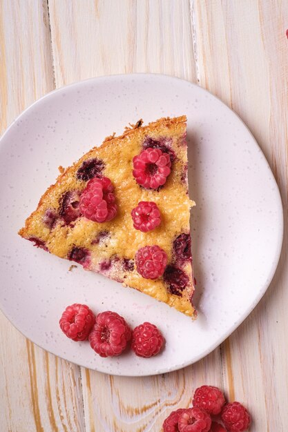 Fatia de torta saborosa e doce com frutas frescas e gelatinosas de framboesa em prato, mesa de madeira, vista superior