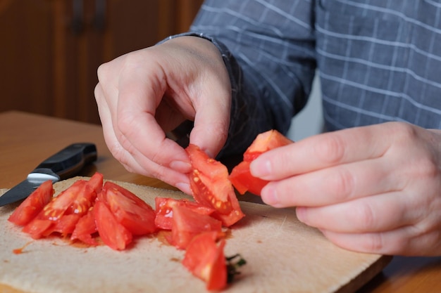 Foto fatiando um tomate vermelho maduro as mãos de uma mulher idosa seguram um tomate para fatiar em uma mesa na cozinha plano aproximado