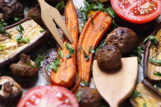 Fatias assadas de berinjela beterraba cenoura cebola batatas cogumelos inteiros especiarias ervas e metades de tomate em papel manteiga closeup de comida vegetariana