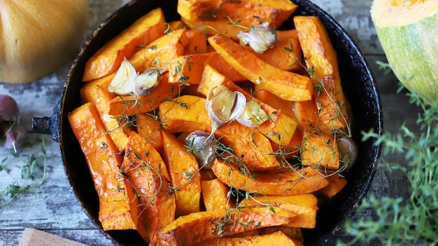 Fatias de abóbora assadas em uma panela com ervas e alho. Almoço de outono. Comida vegana. Lanche saudável.