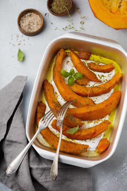 Fatias de abóbora frita com ervas e pimenta, azeite em um concreto cinza ou pedra.