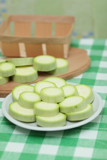 Fatias de abobrinha em um prato branco e uma tábua de madeira em uma toalha de mesa verde Legumes saudáveis Closeup