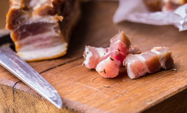 Fatias de bacon defumado cru na placa de madeira com cominho e ervas.