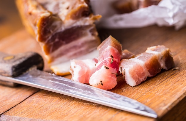 Fatias de bacon defumado cru na placa de madeira com cominho e ervas.