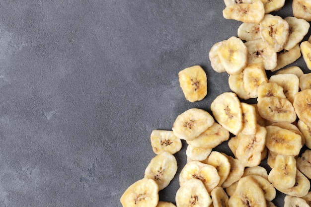 Fatias de banana doce em fundo cinza, vista superior com espaço para texto. Frutas secas como lanche saudável