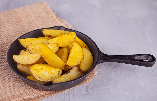 Fatias de batata assada caseira com ervas na panela de ferro preto sobre o fundo cinza