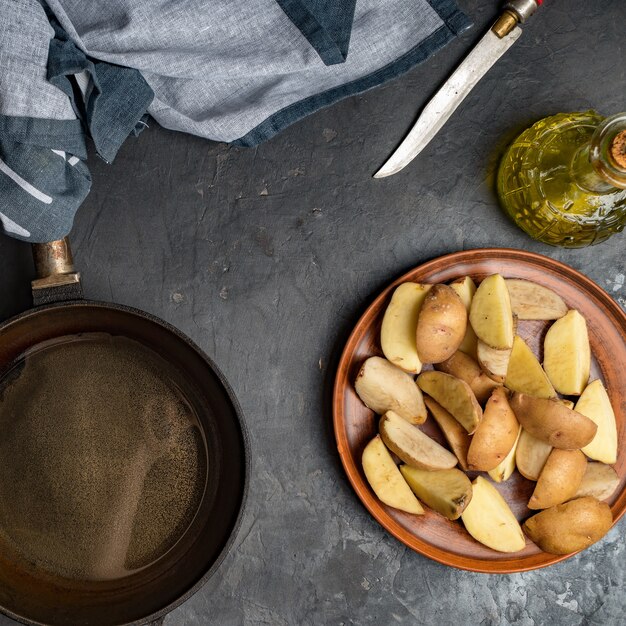 Fatias de batata, frigideira de ferro, faca e óleo