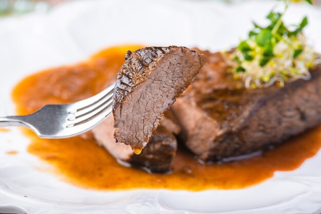 Fatias de bife de bife grelhado malpassado com molho no prato branco. Foco seletivo.