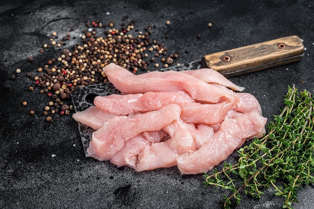 Fatias de carne de aves crua em uma tábua de açougueiro com peito de frango de talhador de carne fundo preto vista superior