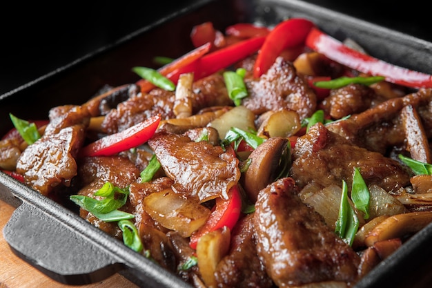 Fatias de carne de porco frita com legumes em uma frigideira preta