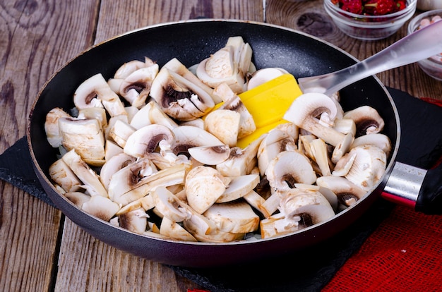 Fatias de champignon crus na frigideira na mesa de madeira.