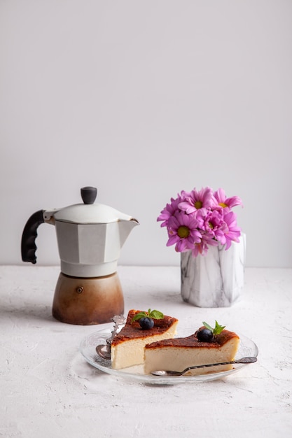 Fatias de cheesecake caseiro basco queimado com mirtilos e folhas de hortelã, cafeteira géiser, flores em um vaso