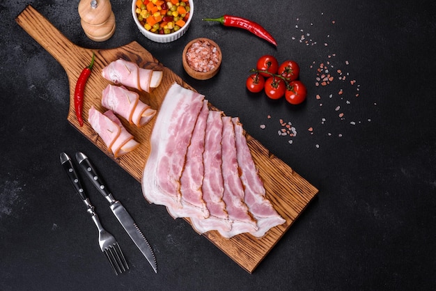 Fatias de delicioso bacon cru ou salgado com especiarias sal legumes e ervas em uma tábua de madeira