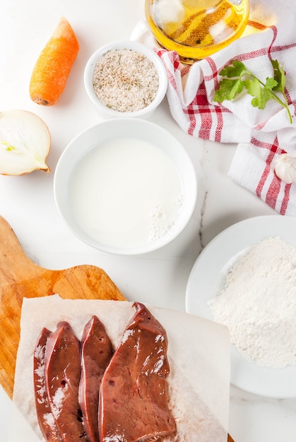 Fatias de fígado bovino cru com especiarias, ervas, leite e farinha, vista superior de mesa de mármore branco