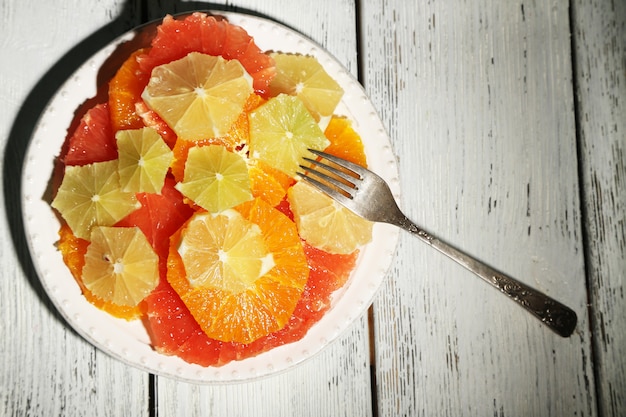 Foto fatias de frutas cítricas no prato, mesa de madeira