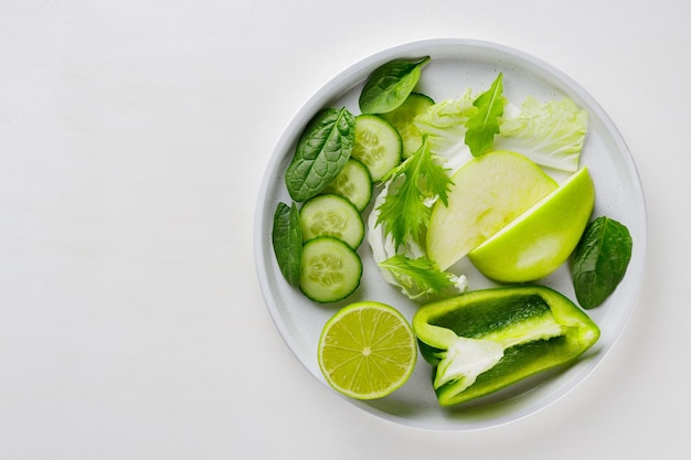 Fatias de frutas e vegetais verdes em um prato branco. Comida de dieta verde fresca sobre fundo branco. Conceito de comida vegetariana saudável. Copie o espaço. Vista do topo