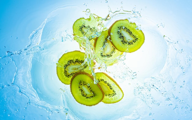 Fatias de kiwi salpicando em água limpa isoladas em fundo azul claro conceito de alimentos saudáveis