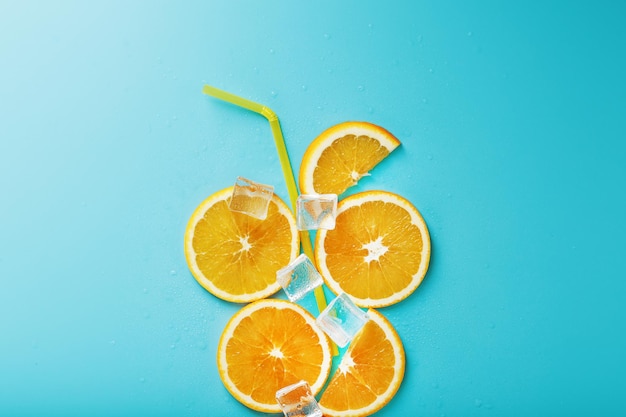 Fatias de laranja e cubos de gelo com um canudo sobre fundo azul em forma de coquetel.