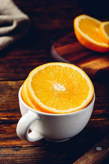 Foto fatias de laranja em um copo branco sobre uma superfície de madeira