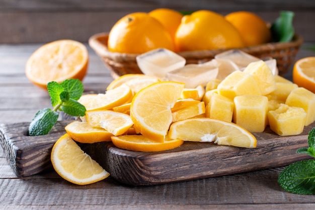 Fatias de limão congeladas e cubos de suco de limão em uma placa de corte sobre uma mesa de madeira, frutas congeladas