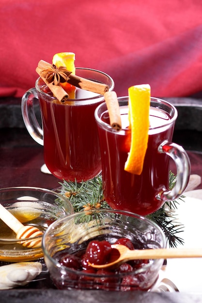 Fatias de mel de abelha de vinho quente vermelho quente de laranjas e especiarias em uma decoração de natal de fundo escuro com galhos de abeto e um guardanapo vermelho