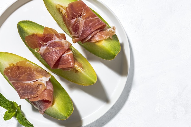 Fatias de melão fresco com presunto com luz do sol em fundos coloridos. Conceito de comida espanhola